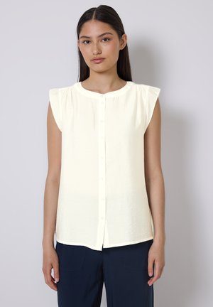 Chemisier à manches courtes, boutonné, en tissu doux de couleur jaune clair. Il présente un col rond et des accents de volants subtils sur les épaules.