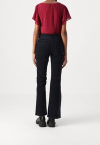 Diepblauwe flared corduroybroeken met subtiele textuur en achterzakken, gecombineerd met een kortere maroon blouse. Zwarte hoge hakken.