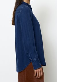 Donkerblauwe blouse met lange mouwen en een volantskraag, zachte textuur, knoopmanchetten en een ronde zoom, gedragen over een bruine rok.