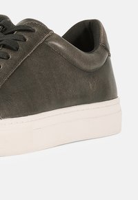 Γκρι δερμάτινο αθλητικό παπούτσι με χαμηλό προφίλ, μαύρα κορδόνια και λευκή λαστιχένια σόλα με υφή.