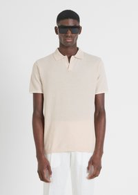 Polo shirt corto a maniche corte di un leggero beige, realizzato in un tessuto texture, con colletto e sottili dettagli a costine sui bordi.