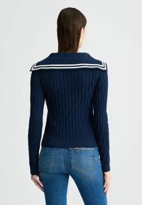 Maglione blu navy a maglia cable con un ampio colletto da marinaretto decorato da strisce bianche. Design aderente con polsini e orlo a coste, abbinato a jeans blu.