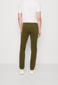 Olivgröna slim-fit byxor med en slät textur, två bakfickor och en liten logodetalj, tillsammans med en enkel vit t-shirt.