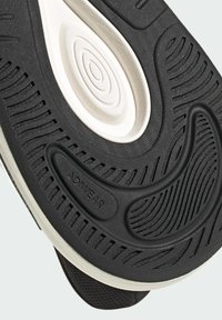 Semelle de chaussure avec une bande de roulement en caoutchouc noir texturé, un détail circulaire blanc sur la semelle intermédiaire, et un marquage "ADIWEAR" sur la zone du talon.