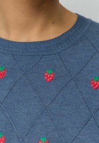 Suéter azul de punto con un patrón de diamante y pequeñas fresas bordadas en rojo y verde en la parte delantera. Cuello redondo.
