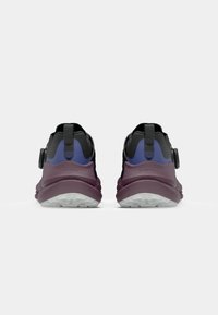 Baskets de sport noires et violettes avec une tige texturée, une languette arrière et une semelle extérieure blanche visible avec un accent violet.