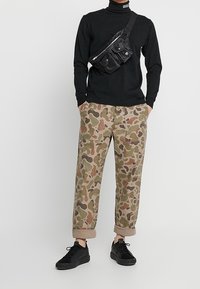 Černý dlouhý rukáv s rolákem, maskáčové volné kalhoty s ohrnutými manžetami a černé tenisky. Křížová taška s několika kapsami.