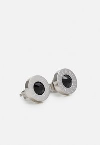Pendientes de aro en tono plateado con una gema negra central, rodeada por un bisel circular con el grabado de la marca.