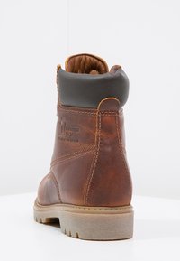 Bottine en cuir marron avec un col doux noir, détails texturés, semelle robuste et logo en relief. Design cousu pour une durabilité accrue.