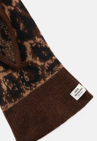 Strikket skjerf i brune toner med leopardmønster og svarte detaljer. Ribbete tekstur nederst og et merke på siden.