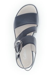 Black leather sandal featuring crisscross straps, a round metallic buckle, and a beige cushioned insole. Flat sole with no visible patterns.