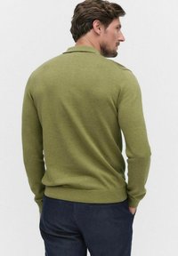 Olivevihreä neulepaita, jossa on pitkät hihat, röyhelökaulukset ja rento istuvuus. Sujuva rakenne, yksinkertainen muotoilu ja ei näkyviä kuvioita.