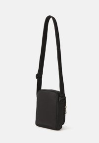 Melnas crossbody somas taisnstūra forma. Izgatavota no mīksta auduma, ar rāvējslēdzēja aizdari un regulējamu siksnu ar logotipa detaļām.