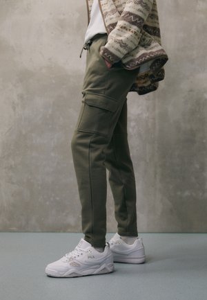 Olivenfarbene Cargo-Hosen mit einem Kordelzugbund, ausgestattet mit Seitentaschen und gestickten Details, kombiniert mit weißen FILA-Sneakern.