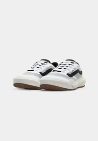 Białe i czarne sportowe sneakersy z grubą podeszwą, pokazane z boku z sznurówkami na jednolitym tle.