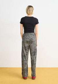 Haut noir à manches courtes associé à un pantalon ample à imprimé léopard avec une taille à cordon. Le modèle porte des chaussures rouges. L'arrière-plan est clair.