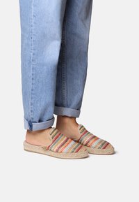Scarpe slip-on intrecciate con strisce multicolori, suola in juta naturale e fodera morbida. Abbinato a pantaloni in denim blu chiaro arrotolati.