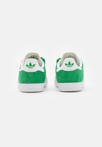 Green suede sneakers with white rubber soles and tongue. Features a white heel tab with a green logo. Texture is soft, and design is low-top.