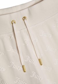 Krämfärgad jogger midja med präglad "Juicy"-mönster, med krämfärgade snörningar och guldfärgade metalländar. Mjuk textur och strukturerad design.