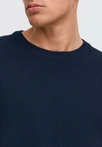 Had navy kék kötött pulóver, bordázott kerek nyakkal. A textúra sima és egységes, amely egy testhezálló fazont mutat be.