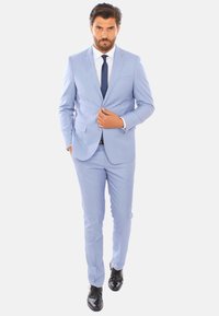 Abito blu chiaro con rever a punte, abbinato a una camicia bianca e una cravatta blu navy. L'individuo indossa scarpe nere lucide. Tessuto liscio.