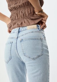 Světle modré džínové kalhoty s designem pěti kapes, rovného střihu, kontrastním prošíváním a viditelnou značkovou nálepkou na zadní straně.