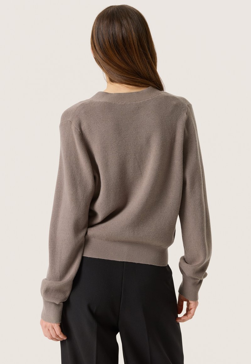 Braun gestrickter Pullover mit lockerer Passform, gerippten Bündchen und Saum, rundem Ausschnitt und subtiler Textur. Getragen mit schwarzen Hosen.