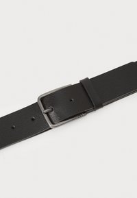 Ceinture en cuir noir avec une surface texturée, boucle en métal argenté et cinq trous pour ajustement. Design simple et fonctionnel.