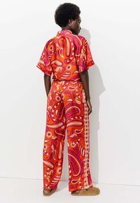 Un ensemble coordonné à motifs rouges se compose d'un haut à manches courtes et d'un pantalon à jambes larges avec des motifs tourbillonnants dans des teintes de rose, blanc et orange.
