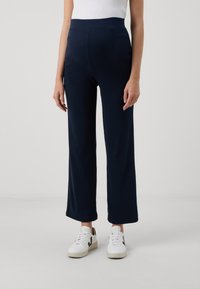 Navy wide-leg trousers with a high ribbed waistband. Made from a soft material, featuring a smooth texture and a relaxed fit. White sneakers worn.