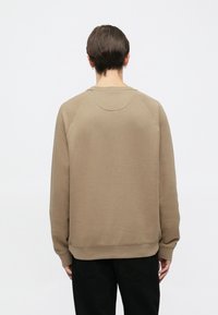 Χακί φούτερ με χαλαρή εφαρμογή, ραγκλάν μανίκια, ριμπ μανσέτες και τελείωμα. Λείο ύφασμα, ελάχιστες λεπτομέρειες και στρογγυλεμένη ραφή στην πλάτη.