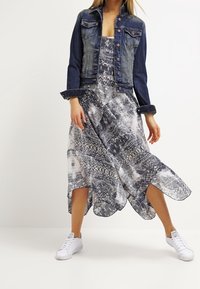 Denimtakki pitkillä hihoilla, napitettu edestä. Valoisa, kuvioitu mekko sinivalkoisena, epäsymmetrisellä helma. Yhdistetty valkoisiin lenkkareihin.