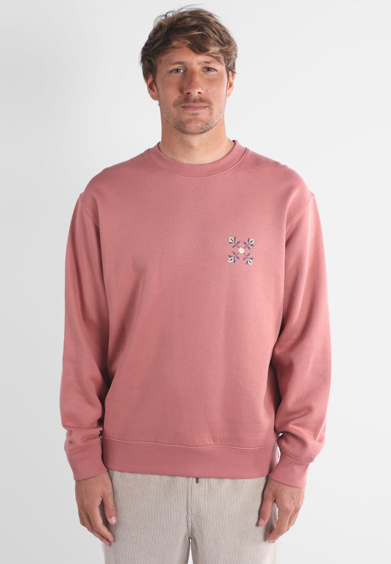 Sweatshirt rose avec col rond, manches longues et poignets côtelés. Présente un motif de broderie florale sur la poitrine. Texture de tissu douce.
