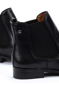 Botas de tobillo de cuero negro con paneles elásticos en los laterales, un acabado suave, punta redonda y un pequeño accent metálico cerca del tobillo.