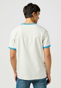 Camiseta de manga corta para hombre, color blanco roto con cuello y bordes de las mangas de rayas azules, hecha de algodón, que presenta un ajuste relajado y una textura suave.