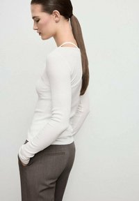Top bianco a maniche lunghe con un motivo a costine abbinato a pantaloni marroni aderenti. Il top presenta un collo a barca e una silhouette slim, che esalta un aspetto elegante.