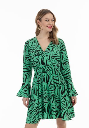 Vihreä mekko, jossa on musta seeprahkakuosi, V-kaula-aukko, elastinen vyötärö ja pitkät kellohihat. Valmistettu kevyestä materiaalista, joka on virtaava.