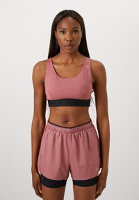 Sports bra and shorts set in dusty pink. Soft fabric with a contrasting black elastic waistband. Bra features a rounded neckline and logo detail.