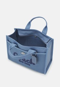 Sac à main en tissu bleu avec deux poignées, poche avant à rabat, poche zippée visible à l'intérieur et logo Coach New York sur le devant.