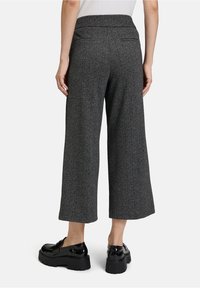Pantalons texturés gris avec un design à jambes larges. Dotés d'une taille haute et de deux poches arrière. Portés avec des chaussures à plateforme noires.