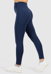 Marina högmidjade leggings tillverkade av stretchigt tyg, med ett texturerat mönster på sidan, kombinerat med vita sportskor.