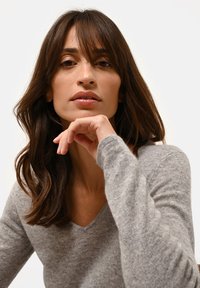 Grijze V-hals trui gemaakt van zacht materiaal, met lange mouwen. De textuur lijkt gebreid, met een ruime pasvorm en minimale details.