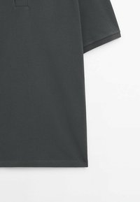 Polo gris foncé à manches courtes en tissu tricoté texturé, présenté du torse à l'ourlet sur fond blanc.
