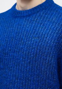 Kék kötött pulóver, vastag, texturált szövettel, kerek nyakkivágással és finom "Obey" logó díszítéssel az elején.