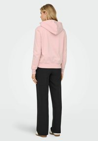 Lys rosa hettegenser med snøring, med ribbestrikket hem og mansjetter. Kombinert med svarte vide bukser og nøytrale sko.