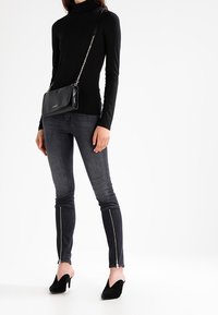 Czarny golf, ciemne dżinsy z zamkami przy kostkach oraz czarne szpilki. Torebka jest czarna z łańcuszkowym paskiem, o fakturowanej powierzchni.