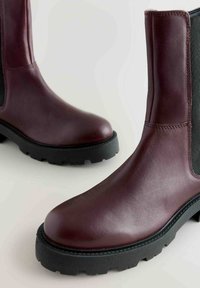 Botine burgundy din piele, cu vârful rotund, panouri elastice pe lateral și talpă din cauciuc texturat negru. Finisaj neted cu detalii de coasere.