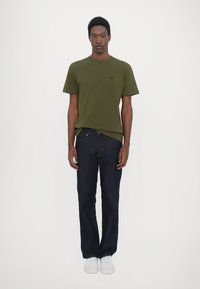 Tricou din bumbac de culoare verde măslin, cu guler rotund, asortat cu blugi negri închis și adidași albi. Design simplu și croială dreaptă.