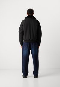 Black bomber jacket with a faux fur collar, paired with dark blue, loose-fitting jeans featuring a subtle faded pattern and back pockets.