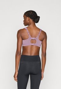 Αθλητικό σουτιέν λεβάντας με κομψό άνοιγμα και ρυθμιζόμενους ιμάντες· συνδυασμένο με μαύρο ψηλόμεσο κολάν. Ομαλή υφή, ελαστικό ύφασμα.